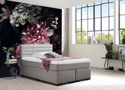 Graues Boxspringbett in modernem Schlafzimmer mit großen Fenstern und floralem Wandbild, seitliche Perspektive