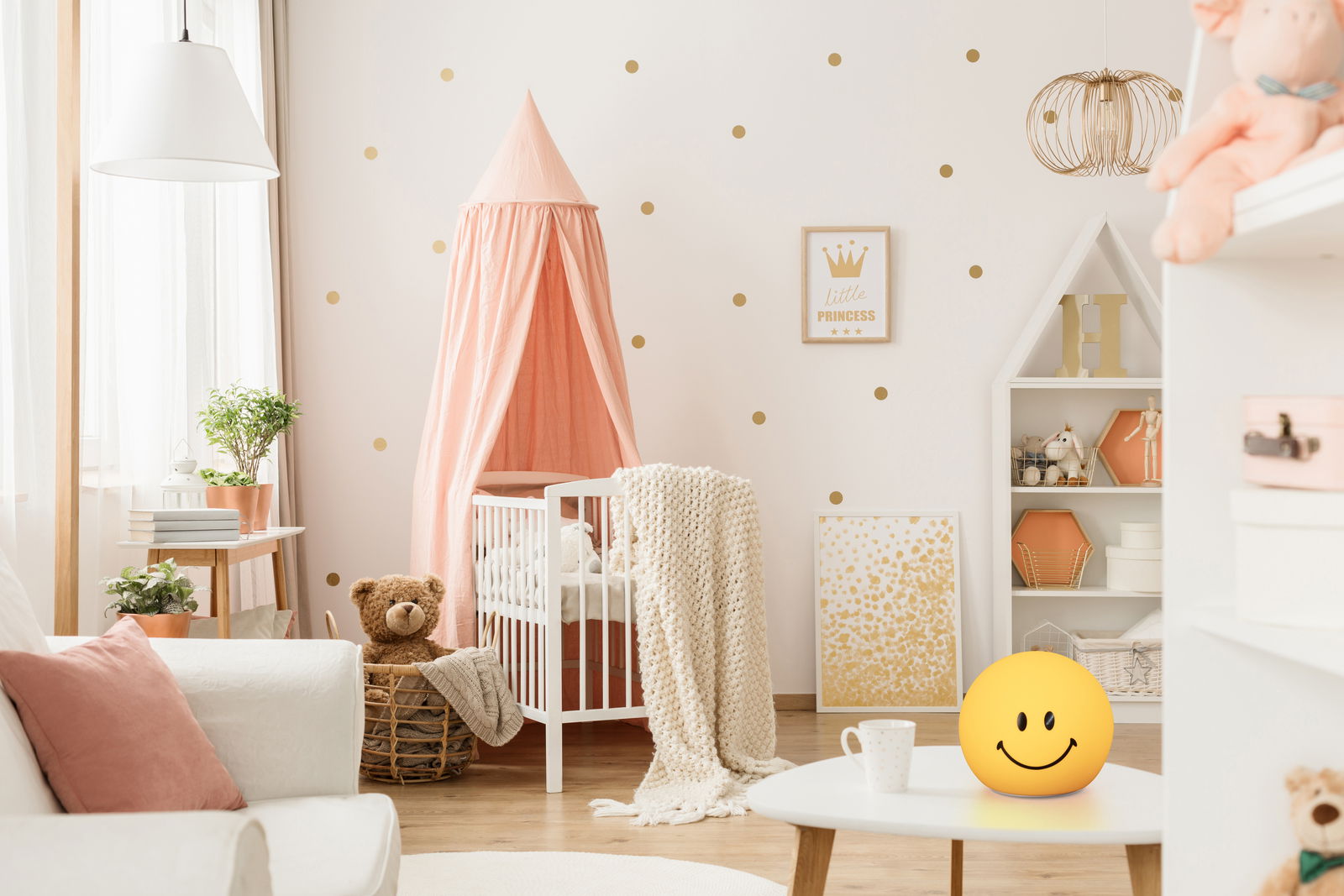 FHL easy Akku-Nachtlicht Smiley GLOWMOJI Akku-Nachtlicht in Form eines gelben Smiley-Gesichts auf einem Tisch in einem gemütlichen Kinderzimmer, seitliche Perspektive.