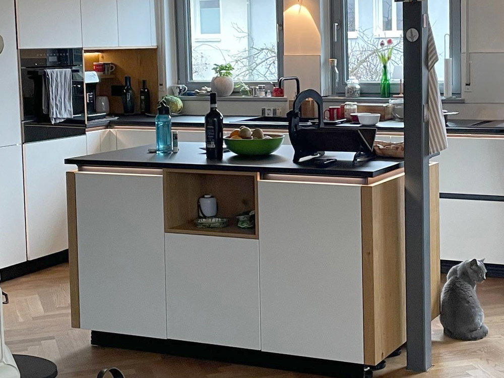 Moderne keuken met kookeiland, fruitschaal en drankjes; een grijze kat zit op de houten vloer.