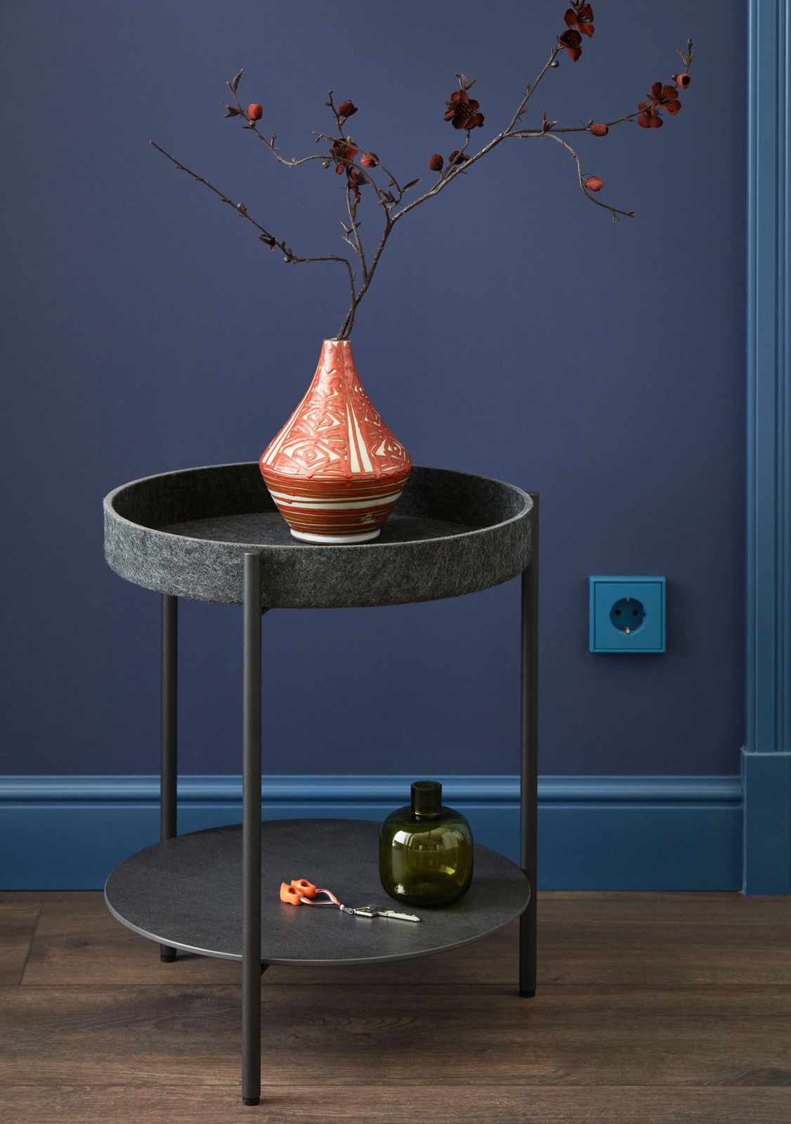 Moderner Beistelltisch mit zwei Ebenen, dekoriert mit einer roten Vase und Zweigen, aus seitlicher Perspektive fotografiert.