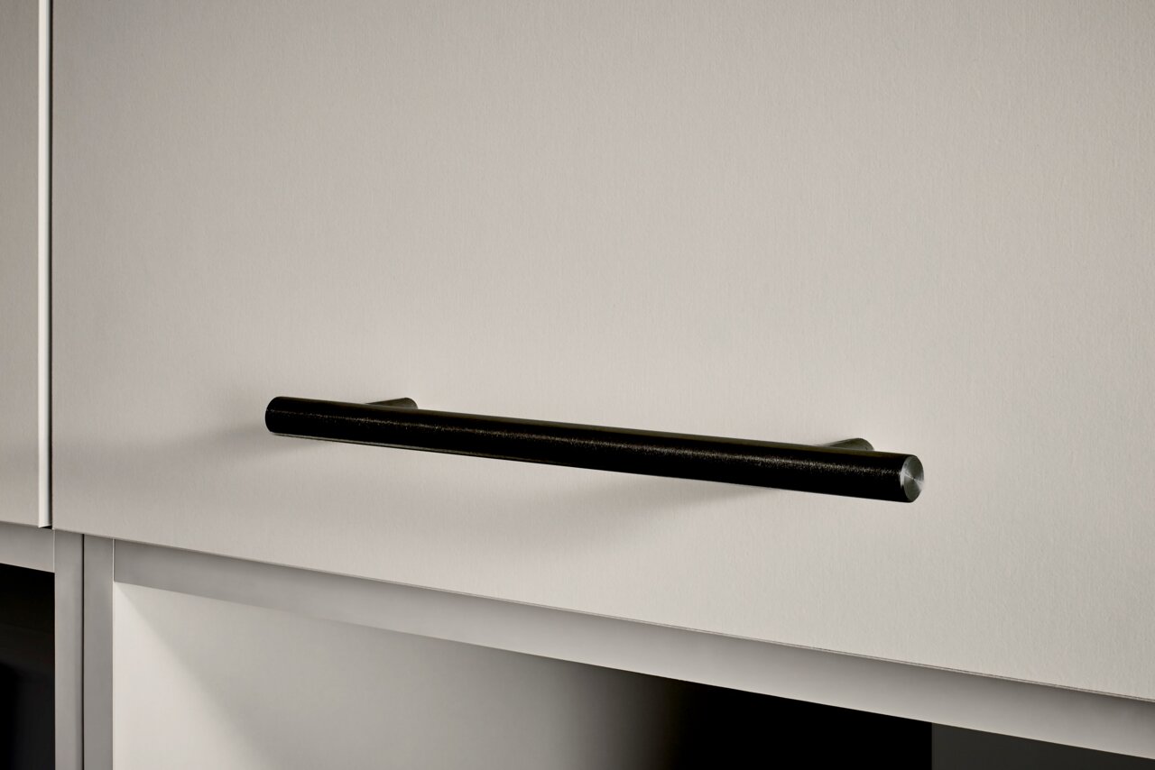 Schwarzer, zylindrischer Möbelgriff aus Metall an einer hellgrauen Schranktür, Frontansicht mit leichter Schrägperspektive von links.