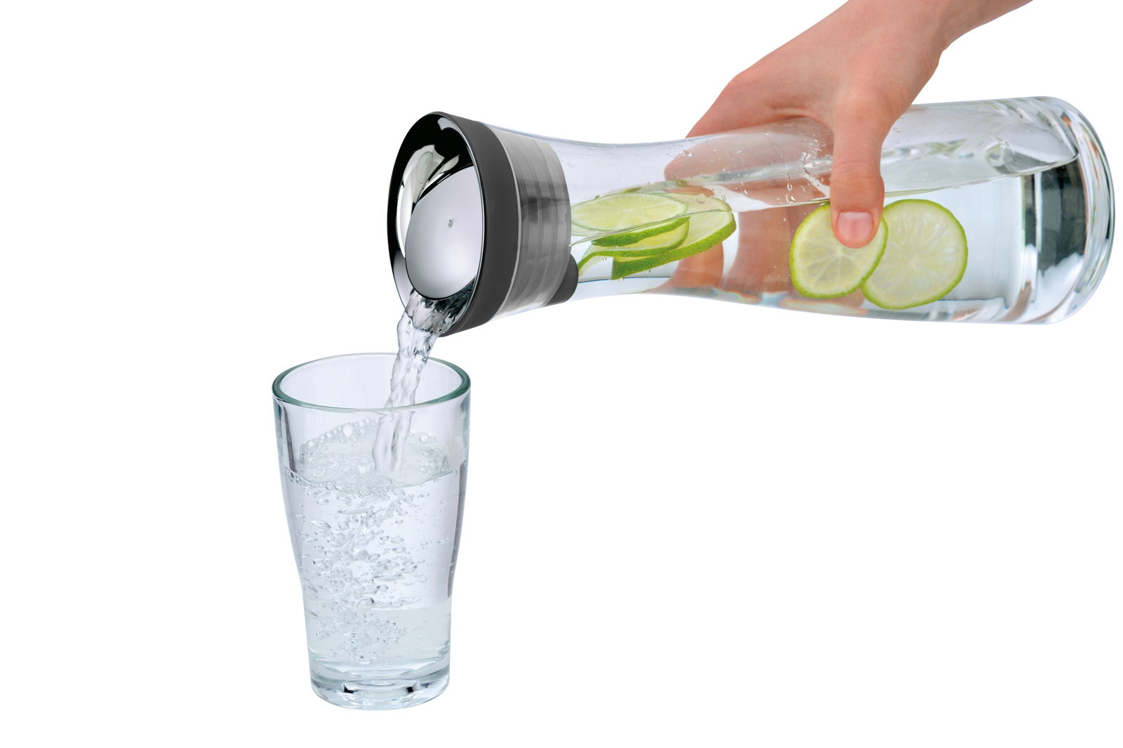 Hand gießt Wasser aus einer Wasserkaraffe BASIC 1L mit Limettenscheiben in ein Glas, seitliche Perspektive