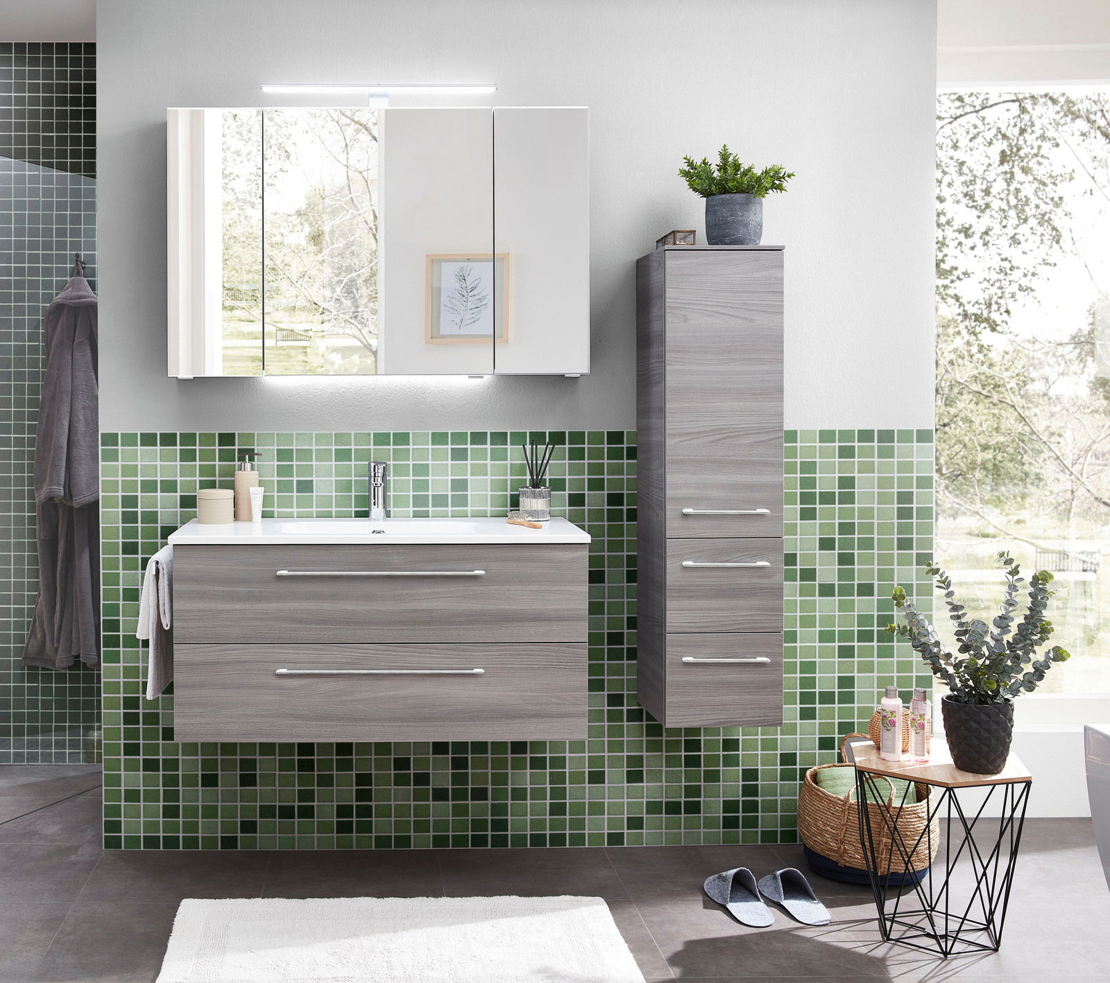 Sadena Badkombination KÖLN Moderne Badkombination mit hängendem Waschtisch und Spiegelschrank in Holzoptik, seitlich ein hoher Schrank, grüne Fliesen im Hintergrund, frontale Perspektive.