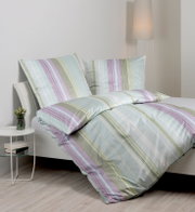 Gestreifte Bettwäsche in Pastelltönen (Mint, Grün, Lila und Weiß) auf einem Bett, schräg von vorne aufgenommen; Deckenbezug und zwei Kissenbezüge im Schlafzimmer-Setting.