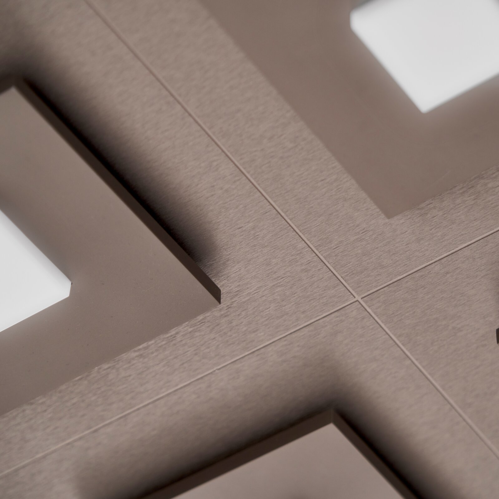 Grossmann LED-Deckenleuchte PLANO Schräge Nahaufnahme einer taupefarbenen, gebürsteten Metalloberfläche mit präzisen Kreuzlinien und geometrischen Aussparungen