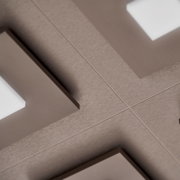 Schräge Nahaufnahme einer taupefarbenen, gebürsteten Metalloberfläche mit präzisen Kreuzlinien und geometrischen Aussparungen