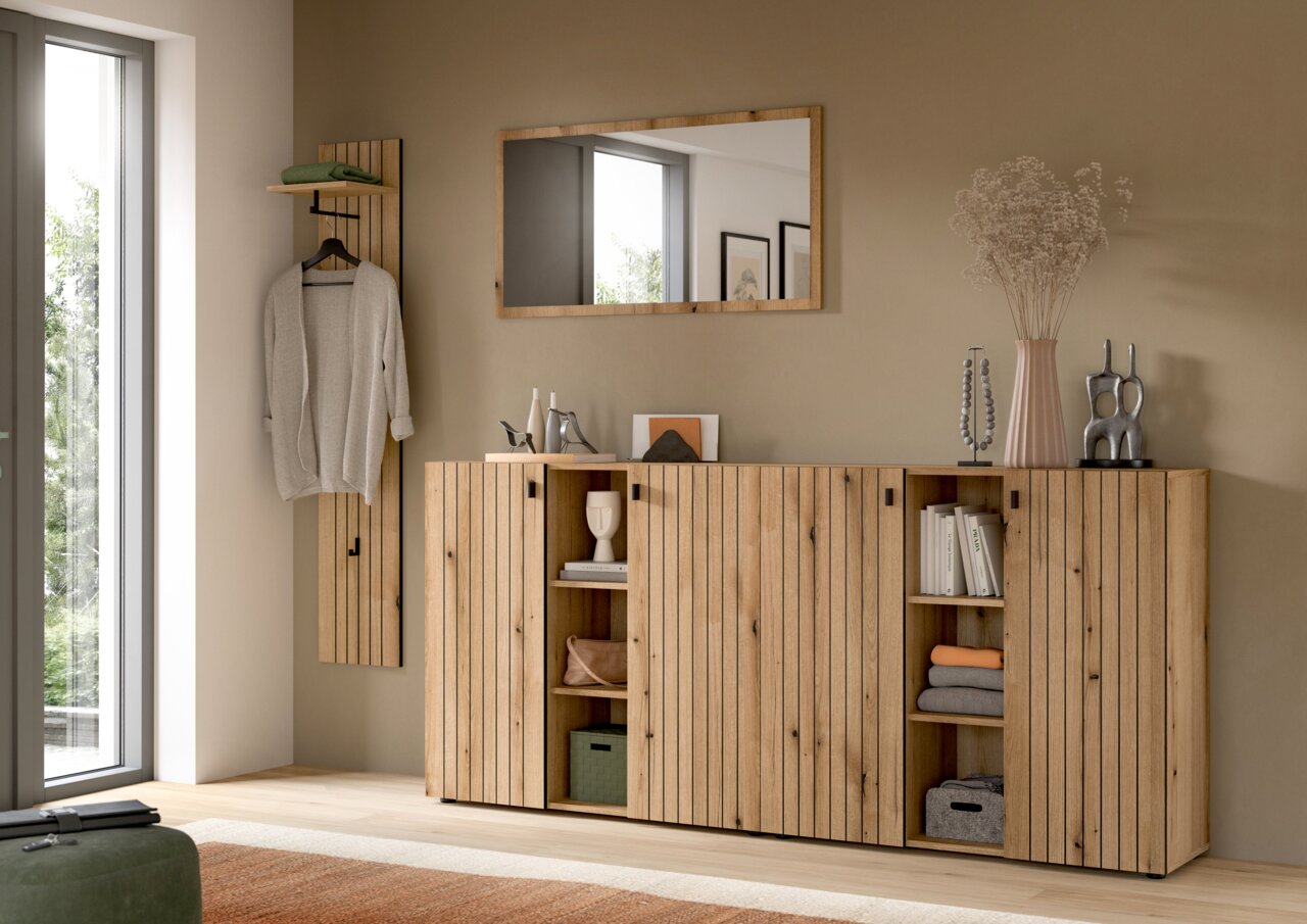 Modernes Sideboard aus hellem Holz mit Lamellenfront und offenen Regalfächern im Flur, darüber rechteckiger Wandspiegel; Ansicht schräg von vorne.