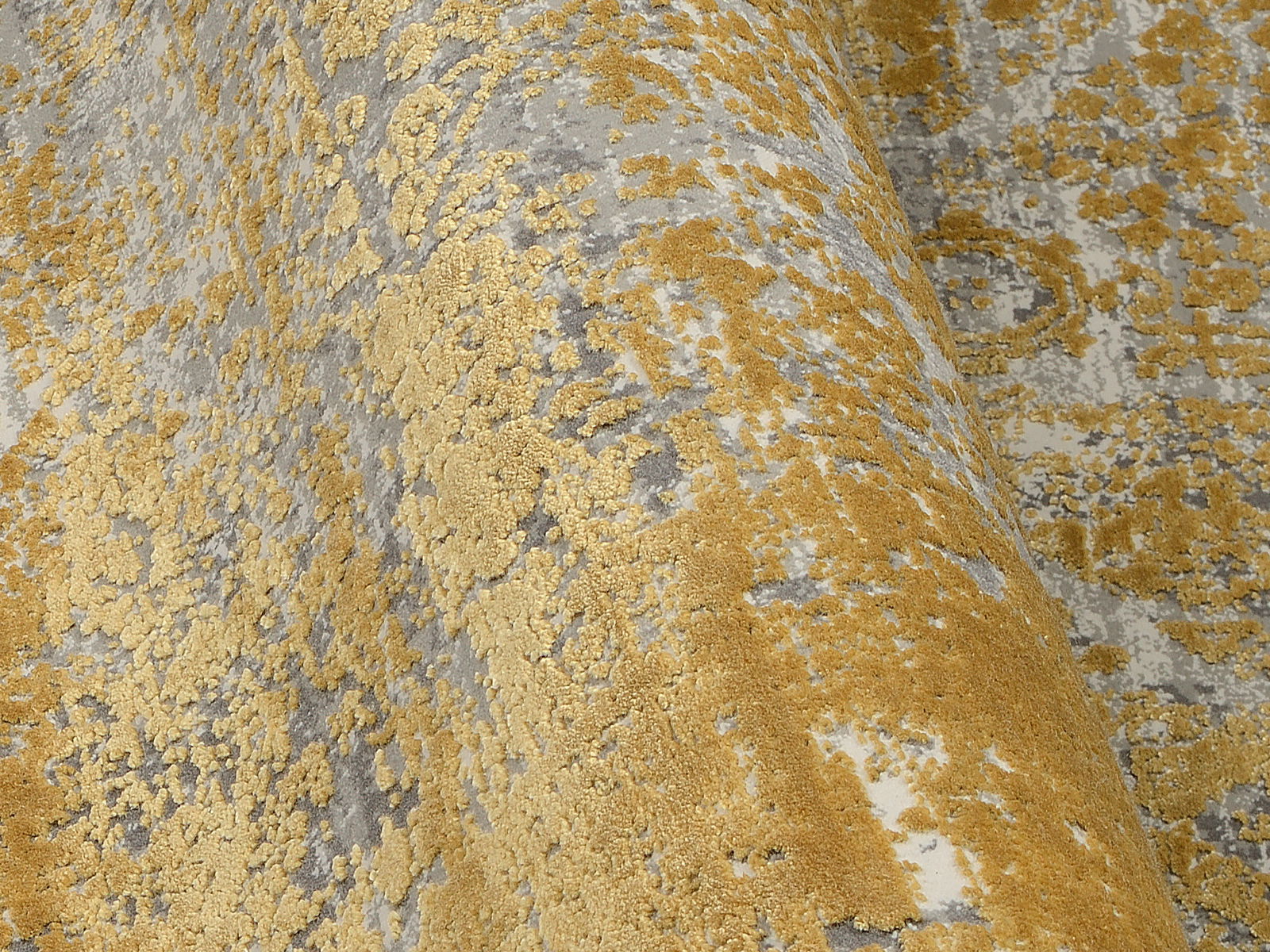 Nahaufnahme eines Designer Teppichs mit goldenen und grauen Mustern, perspektivisch von der Seite aufgenommen.