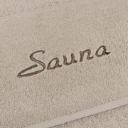 Nahaufnahme eines beigen Saunatuchs mit dem gestickten Wort 'Sauna'.