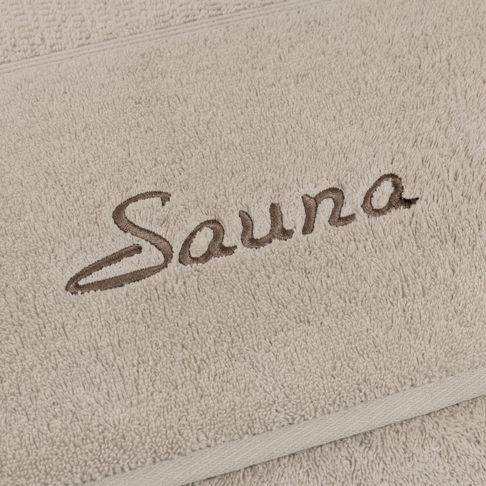 Nahaufnahme eines beigen Saunatuchs mit dem gestickten Wort 'Sauna'.