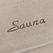 Nahaufnahme eines beigen Saunatuchs mit dem gestickten Wort 'Sauna'.