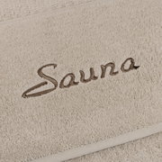 Nahaufnahme eines beigen Saunatuchs mit dem gestickten Wort 'Sauna'.