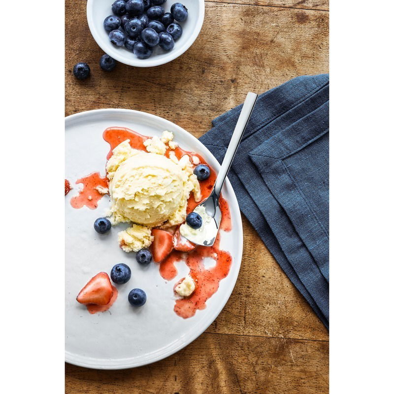WMF Eisschaufel 6-tlg. NUOVA Vogelperspektive auf einen Teller mit einer Kugel Vanilleeis, umgeben von Erdbeersauce und frischen Blaubeeren, daneben eine Eisschaufel.