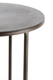 Nahaufnahme eines runden Beistelltisches mit metallischer Oberfläche und schlanken Beinen, seitliche Perspektive.