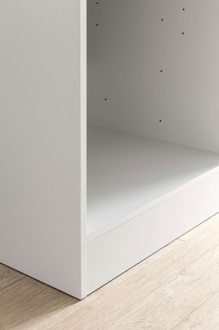 Nahaufnahme eines weißen Küchenschranks mit offener Vorderseite, seitlicher Perspektive auf hellem Holzboden.