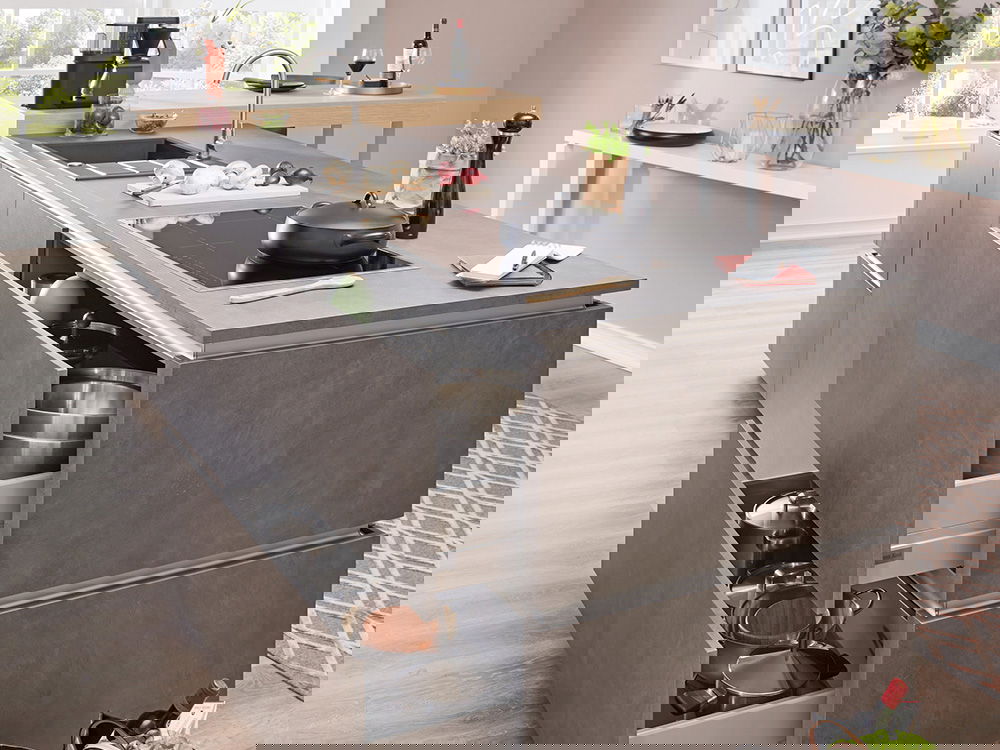 Moderne Kücheninsel mit schlichten grauen Schränken, offenen Schubladen mit Kochutensilien und einem minimalistischen Design.