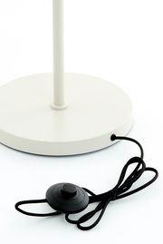 Nahaufnahme der Basis einer weißen Stehleuchte mit schwarzem Fußschalter und Kabel, von oben betrachtet.