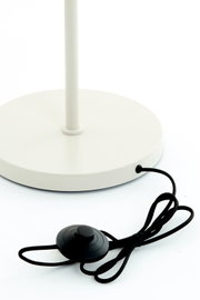 Close-up van de voet van een witte staande lamp met een zwarte voetschakelaar en kabel, gezien van bovenaf.