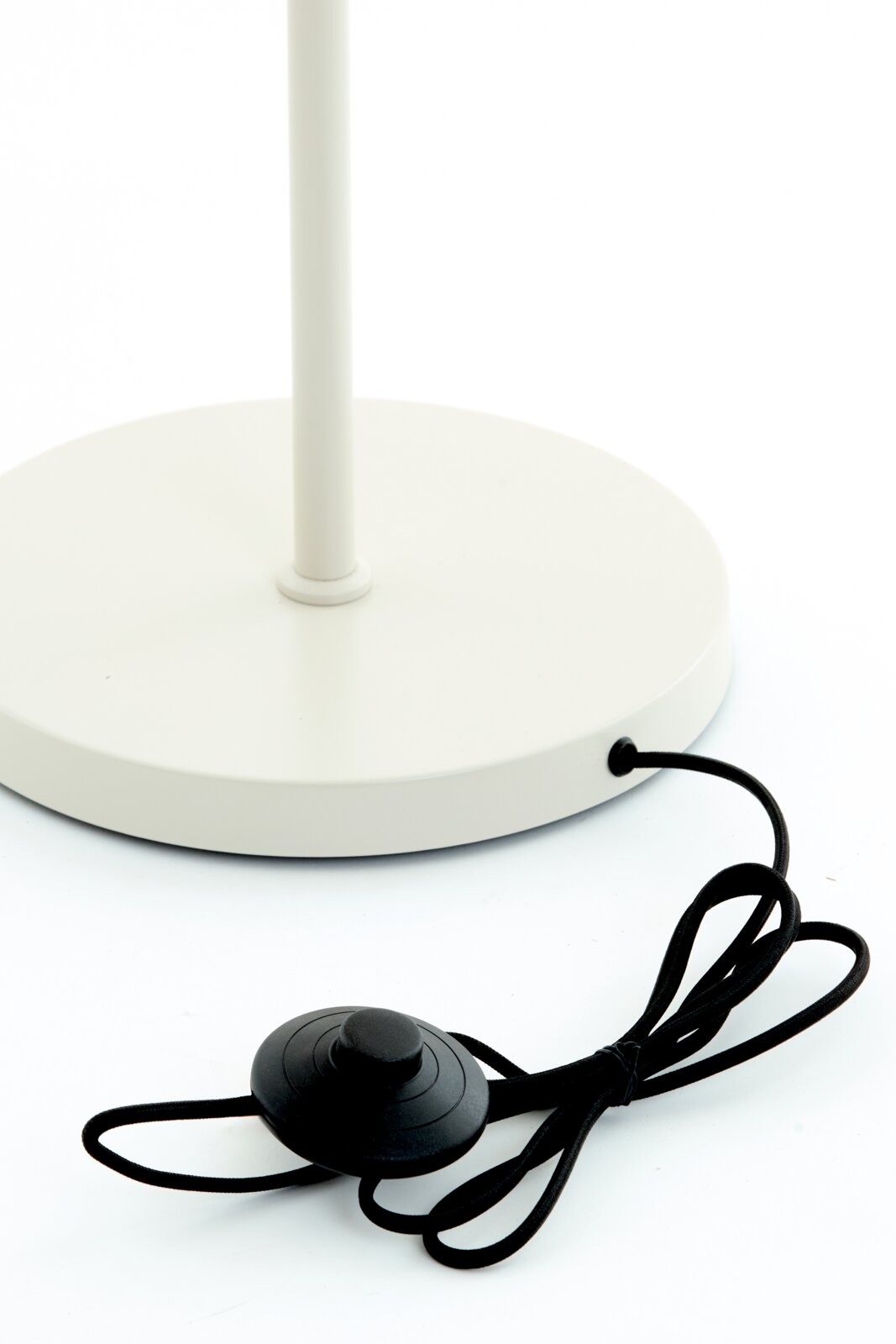 Close-up van de voet van een witte staande lamp met een zwarte voetschakelaar en kabel, gezien van bovenaf.