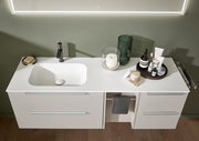 Modernes weißes Badezimmer-Waschtischmöbel mit integrierter Waschschale und schwarzer Armatur, dekoriert mit Kerze, Vase und Pflegeprodukten, Ansicht von vorne leicht von oben
