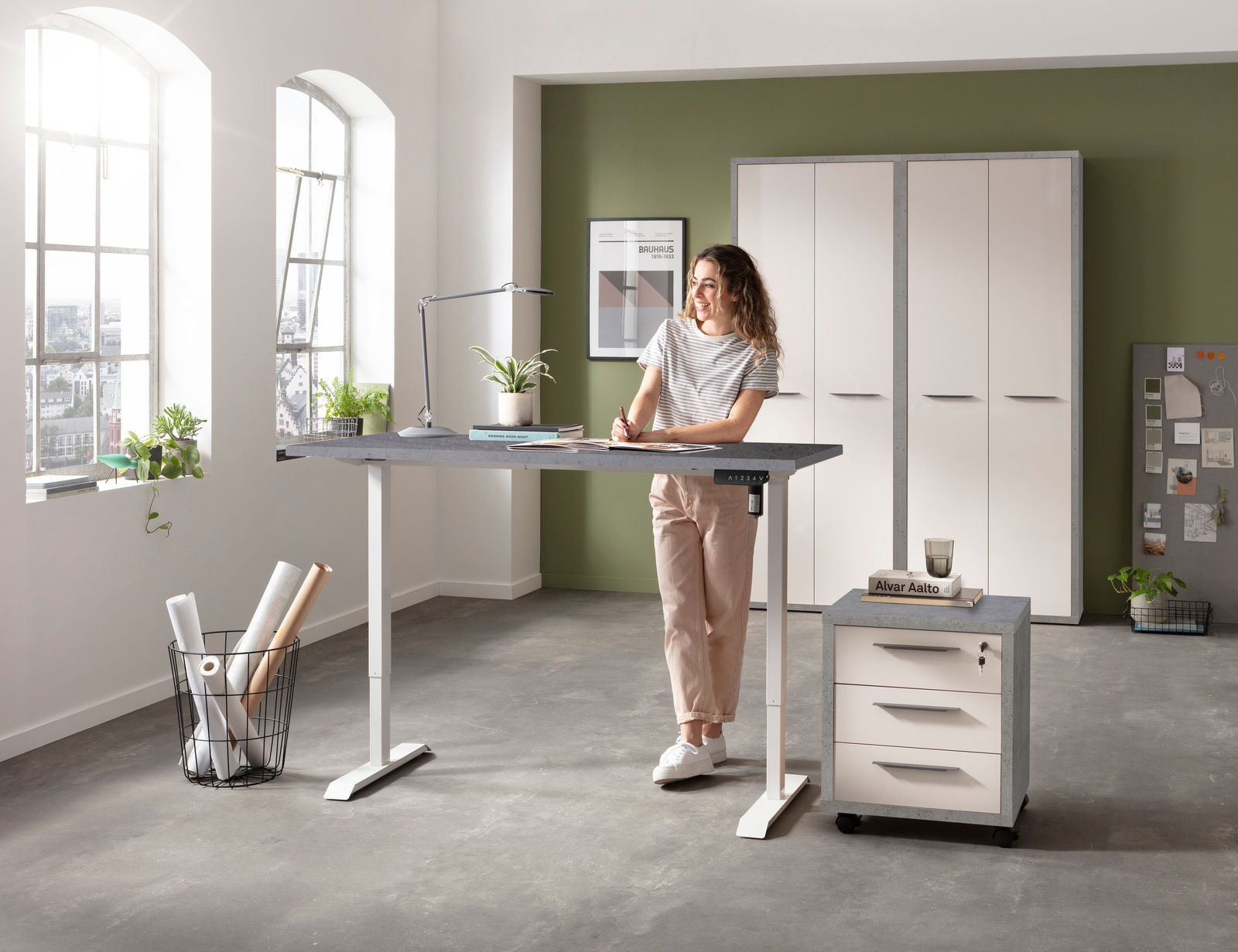 Moderner höhenverstellbarer Schreibtisch in einem hellen Büro mit einer Frau, die daran arbeitet. Perspektive von vorne.