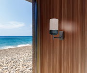 Moderne Akku-Wandleuchte an einer Holzwand mit Blick auf das Meer im Hintergrund.