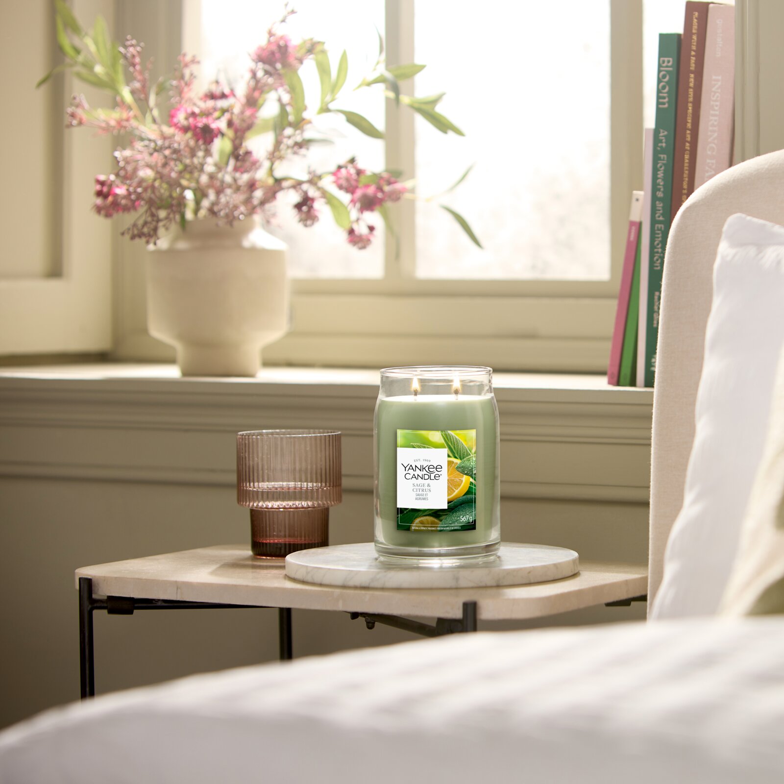Frontalansicht einer brennenden Yankee Candle Sage & Citrus mit zwei Dochten im großen Glas, dekorativ auf einem Beistelltisch in einem hellen Wohnraum inszeniert