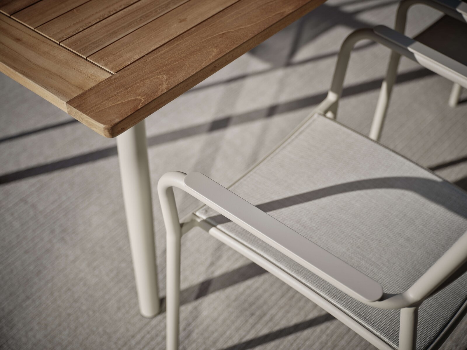 Nahaufnahme eines Stapelsessels mit hellem Metallrahmen und Textilbespannung neben einem Holztisch, von oben betrachtet.