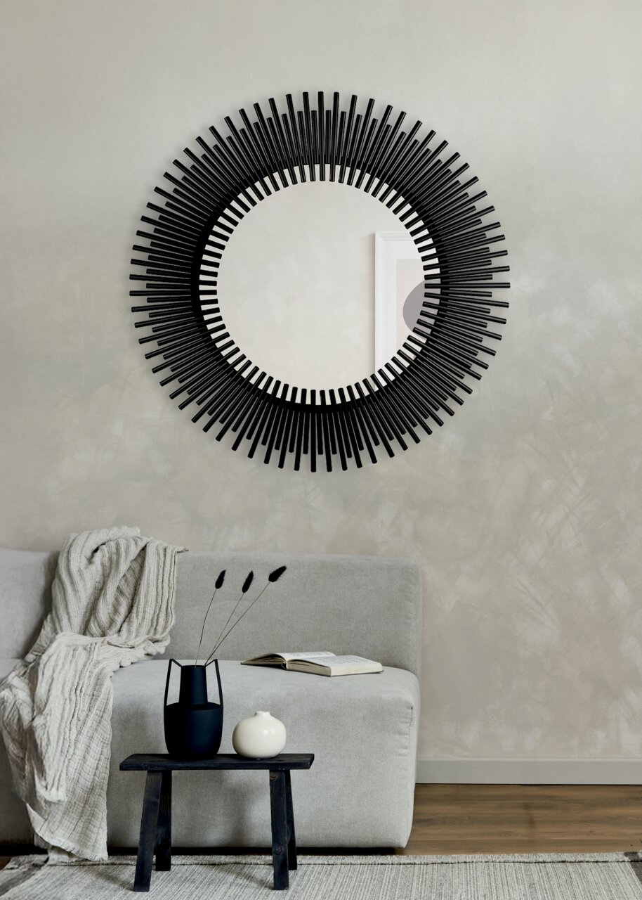 Runder Spiegel mit schwarzem, strahlenförmigem Rahmen, an einer Wand über einem Sofa angebracht, aus frontaler Perspektive betrachtet.
