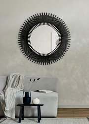 Runder Spiegel mit schwarzem, strahlenförmigem Rahmen, an einer Wand über einem Sofa angebracht, aus frontaler Perspektive betrachtet.