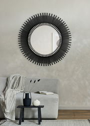 Runder Spiegel mit schwarzem, strahlenförmigem Rahmen, an einer Wand über einem Sofa angebracht, aus frontaler Perspektive betrachtet.