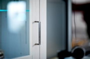 Close-up van een moderne metalen meubelgreep op een witte kastdeur met glazen front, zijaanzicht