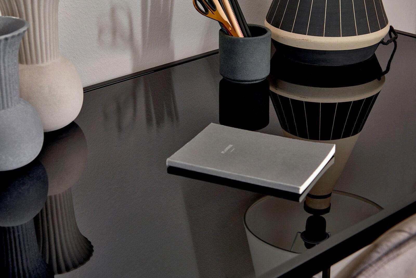 Nahaufnahme eines eleganten Schreibtischs mit glänzender schwarzer Oberfläche, dekoriert mit einer Vase, einem Stifthalter und einem Notizbuch.