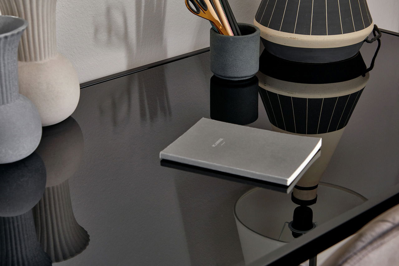 Nahaufnahme eines eleganten Schreibtischs mit glänzender schwarzer Oberfläche, dekoriert mit einer Vase, einem Stifthalter und einem Notizbuch.