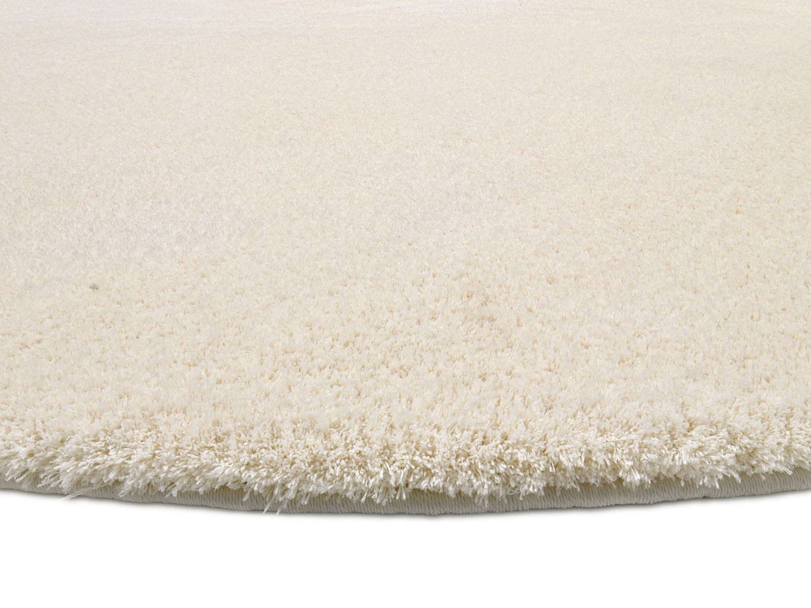 Nahaufnahme eines runden, cremefarbenen Teppichs mit weicher, flauschiger Oberfläche, seitliche Perspektive.