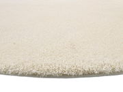 Nahaufnahme eines runden, cremefarbenen Teppichs mit weicher, flauschiger Oberfläche, seitliche Perspektive.