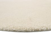 Nahaufnahme eines runden, cremefarbenen Teppichs mit weicher, flauschiger Oberfläche, seitliche Perspektive.