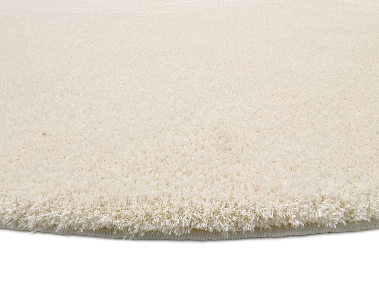 Nahaufnahme eines runden, cremefarbenen Teppichs mit weicher, flauschiger Oberfläche, seitliche Perspektive.