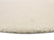 Nahaufnahme eines runden, cremefarbenen Teppichs mit weicher, flauschiger Oberfläche, seitliche Perspektive.