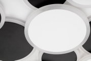Nahaufnahme einer modernen runden LED-Deckenleuchte mit weißer Diffusorfläche und silbernem Rand, von schräg oben fotografiert, vor dunklem Hintergrund