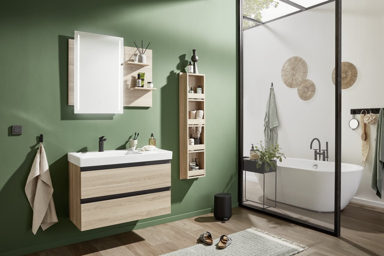 Novel Badkombination NV.074 Moderne Badkombination mit Holz- und Schwarzakzenten, bestehend aus einem Waschtisch mit Spiegel und Regalen, in einem stilvollen Badezimmer mit grüner Wand und freistehender Badewanne. Perspektive: Frontalansicht.