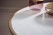 Nahaufnahme eines Couchtischs mit weißer Marmoroptik und goldfarbenem Rand, darauf stehen zwei dekorative Glasgefäße. Perspektive von oben.