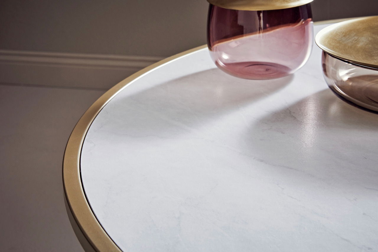 Nahaufnahme eines Couchtischs mit weißer Marmoroptik und goldfarbenem Rand, darauf stehen zwei dekorative Glasgefäße. Perspektive von oben.