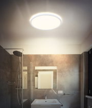 Runde, flache LED-Deckenleuchte mit warmweißem Licht in modernem Badezimmer, Aufnahme aus Untersicht nach oben zur Decke