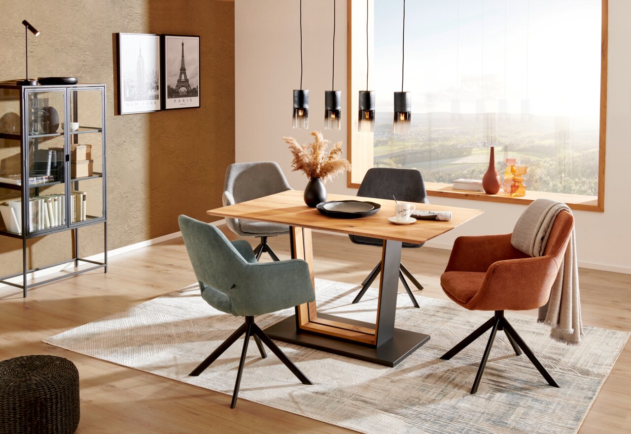 Moderner Esstisch aus Holz mit Metallgestell, umgeben von stilvollen Stühlen in einem hellen, gemütlichen Raum mit großen Fenstern. Perspektive: seitlich.