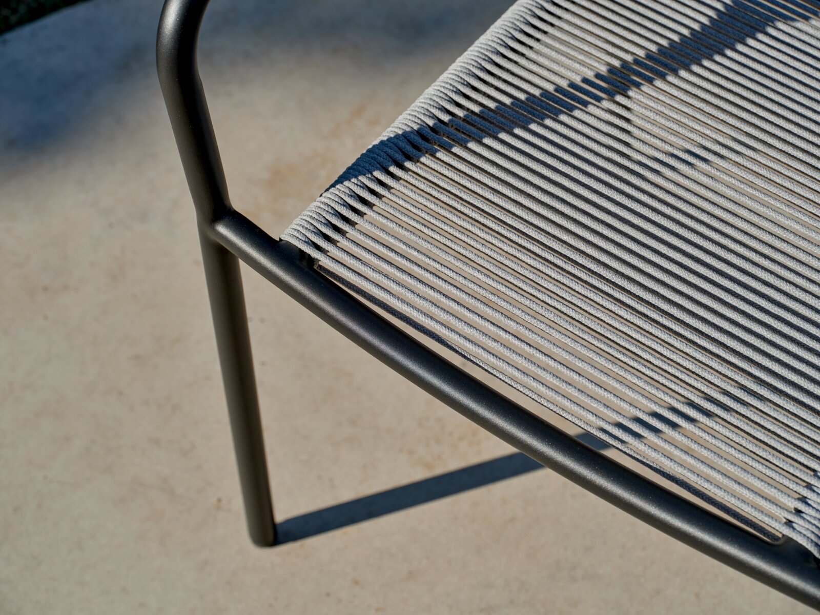 Close-up van een stapelstoel met een zwart metalen frame en grijze kabelbekleding, gezien van bovenaf.