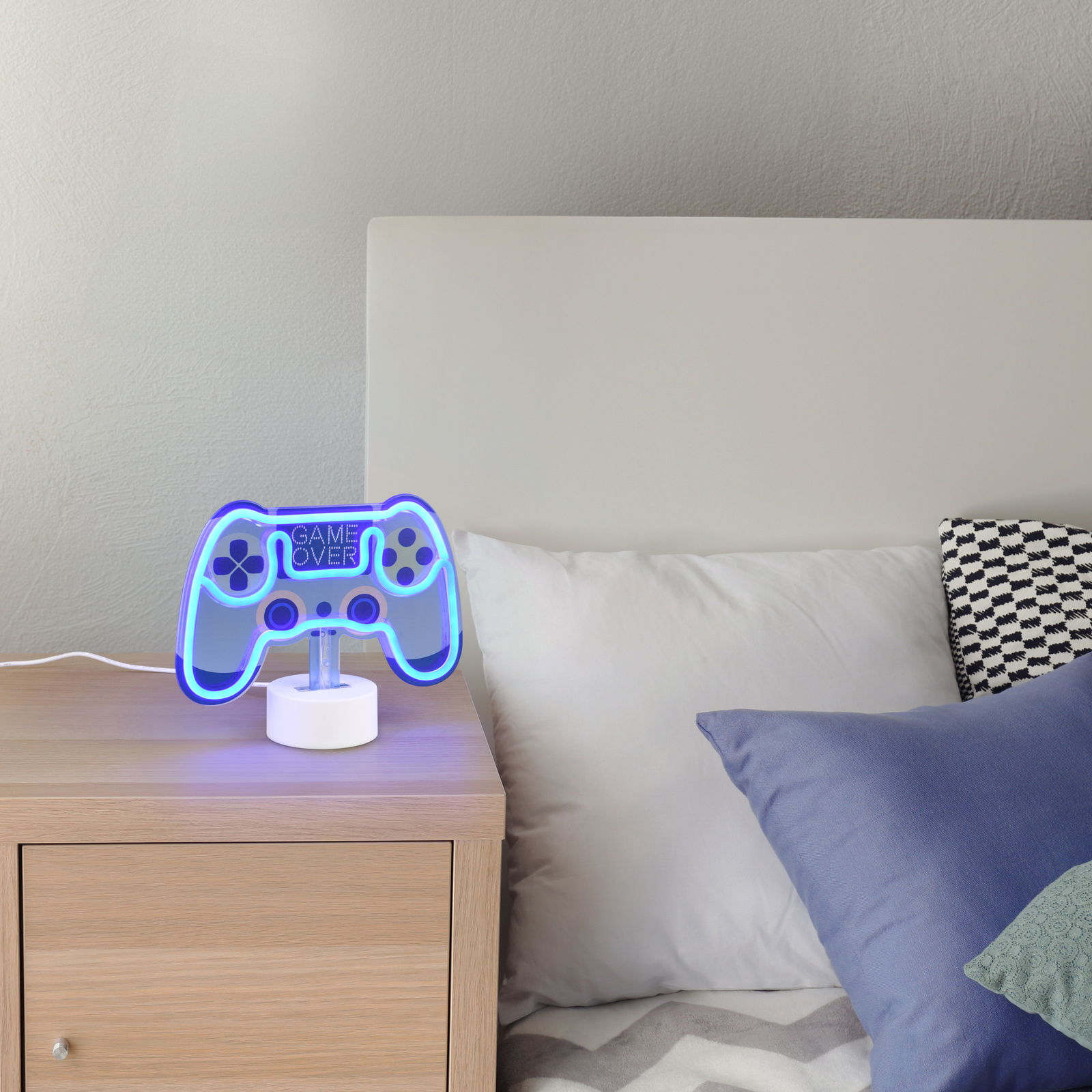 Reality Leuchten Tischleuchte CONTROL Tischleuchte in Form eines blauen Game-Controllers mit der Aufschrift 'Game Over', auf einem Nachttisch neben einem Bett platziert, seitliche Perspektive.