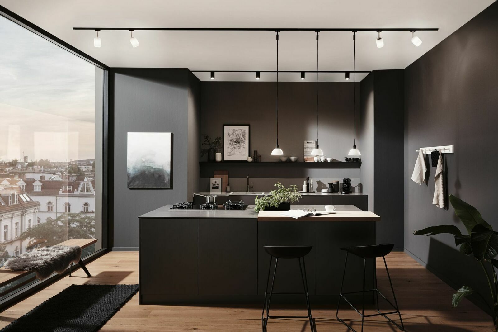 Moderne Küche mit Schienenspot-Beleuchtung von oben, Blick auf die Kücheninsel und große Fenster mit Stadtblick.