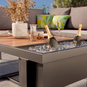 Nahaufnahme eines modernen Lounge-Sets mit einem Tisch, der eine integrierte Kühlbox mit Eis und Champagnerflaschen enthält. Im Hintergrund sind gemütliche Kissen und Dekorationen zu sehen.