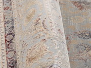 Nahaufnahme eines Orientteppichs mit floralen Mustern in Beige, Blau und Rot, perspektivisch von der Seite aufgenommen.